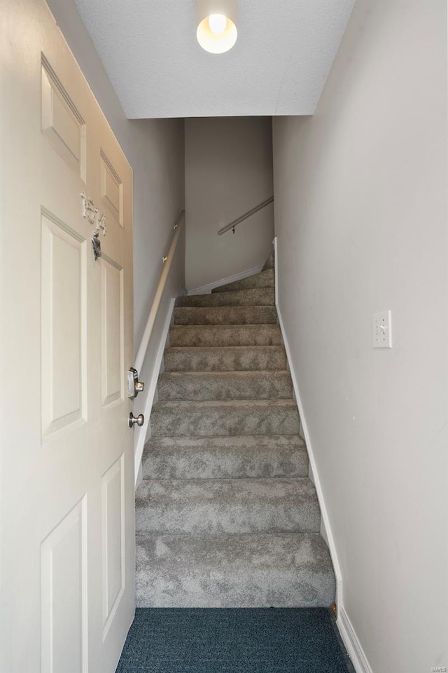 stairway featuring baseboards and carpet flooring