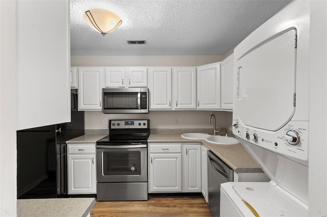 kitchen featuring a sink, white cabinetry, appliances with stainless steel finishes, and stacked washing maching and dryer