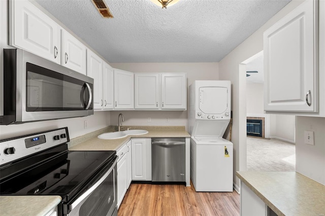 kitchen featuring white cabinets, stacked washer and dryer, appliances with stainless steel finishes, and a sink