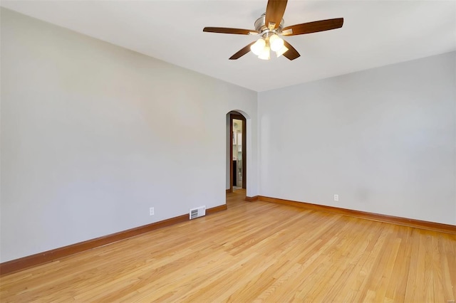 spare room featuring ceiling fan, visible vents, arched walkways, light wood-type flooring, and baseboards