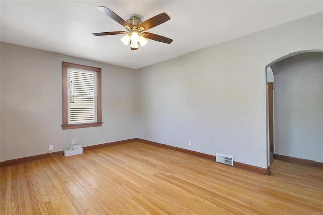 unfurnished room with arched walkways, light wood-style flooring, a ceiling fan, baseboards, and visible vents
