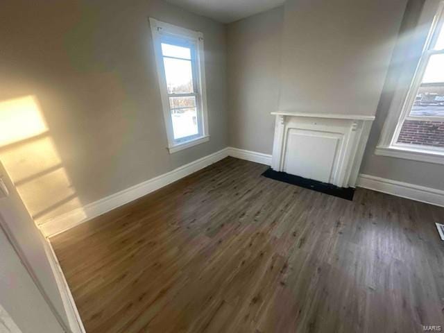 unfurnished living room featuring baseboards, plenty of natural light, and dark wood-type flooring