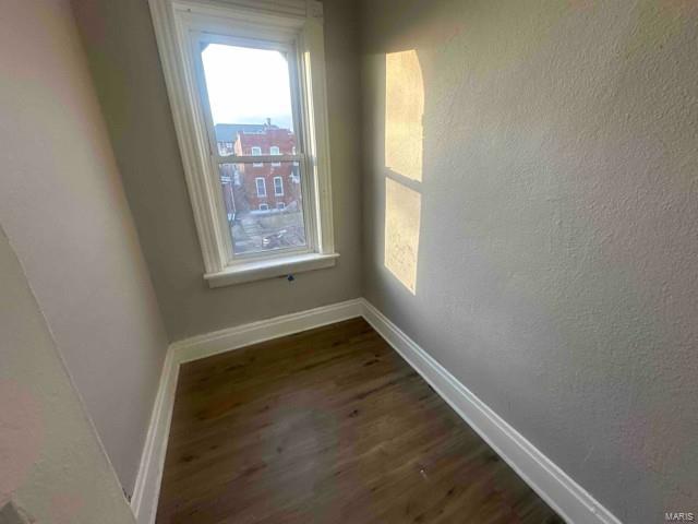 empty room with baseboards, a textured wall, and dark wood-style flooring