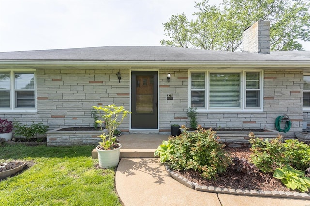 entrance to property with a yard, stone siding, and a chimney