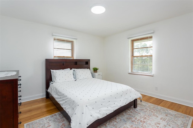 bedroom with baseboards, multiple windows, and wood finished floors