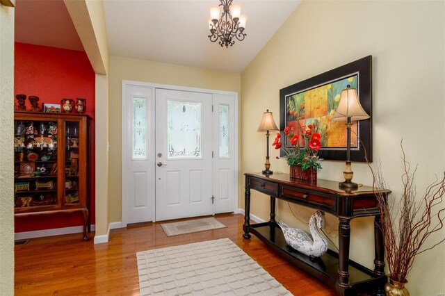 entryway with baseboards, a chandelier, wood finished floors, and lofted ceiling