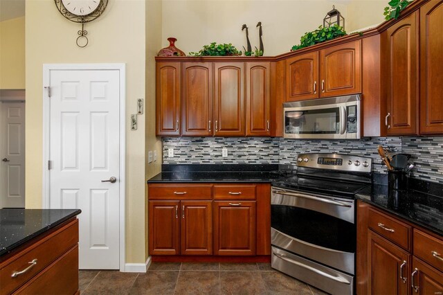 kitchen featuring baseboards, dark tile patterned floors, tasteful backsplash, dark stone countertops, and appliances with stainless steel finishes