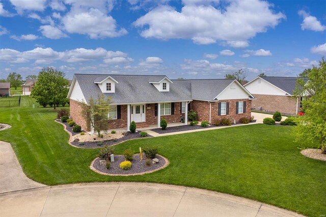 new england style home with a porch, brick siding, a shingled roof, and a front yard