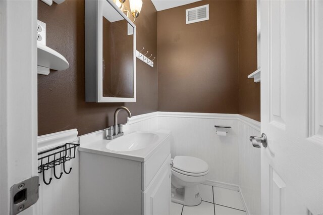 half bath with wainscoting, tile patterned flooring, vanity, toilet, and visible vents