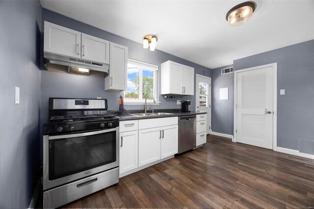 kitchen featuring visible vents, dark countertops, under cabinet range hood, a sink, and stainless steel appliances