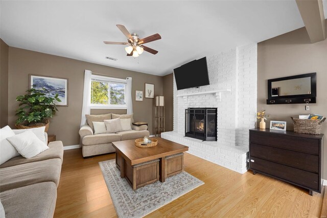 living room featuring a ceiling fan, visible vents, a fireplace, baseboards, and light wood finished floors