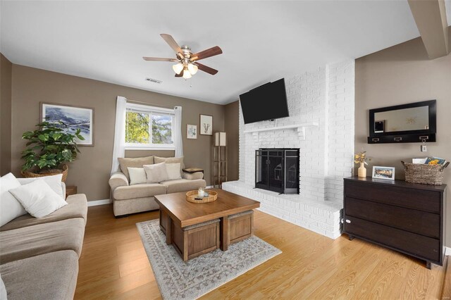 living area with visible vents, a fireplace, baseboards, ceiling fan, and light wood finished floors