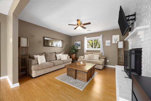 living room featuring visible vents, a brick fireplace, baseboards, a ceiling fan, and light wood-style flooring