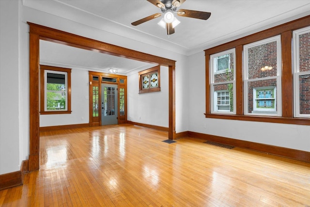 spare room with visible vents, light wood finished floors, crown molding, a ceiling fan, and baseboards