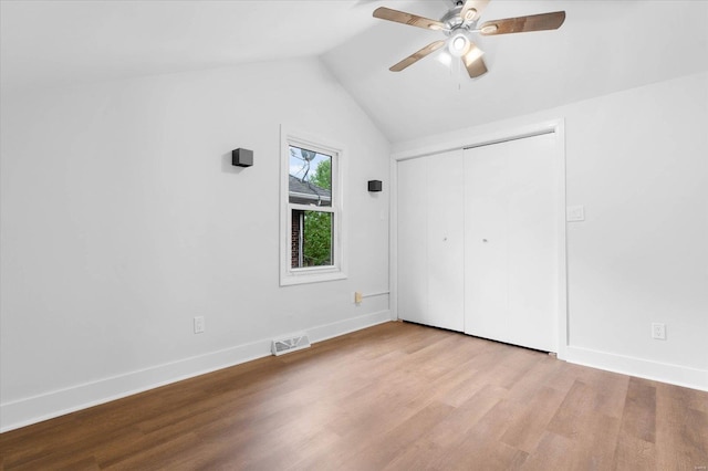 unfurnished bedroom featuring a closet, wood finished floors, visible vents, vaulted ceiling, and baseboards