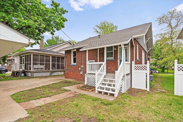 view of front of house with a sunroom, a shingled roof, brick siding, and a front lawn