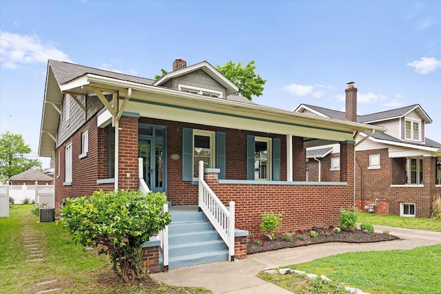 bungalow-style house with a porch, a chimney, central air condition unit, and brick siding
