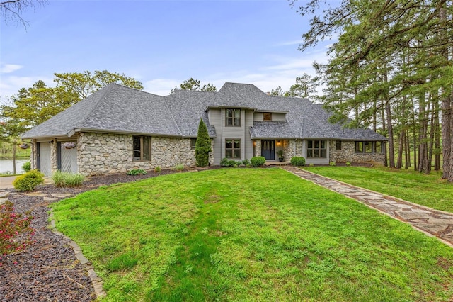 view of front facade with roof with shingles, an attached garage, a front yard, and stone siding