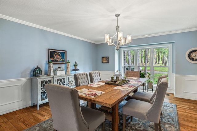 dining space with crown molding, a wainscoted wall, a chandelier, a decorative wall, and hardwood / wood-style floors