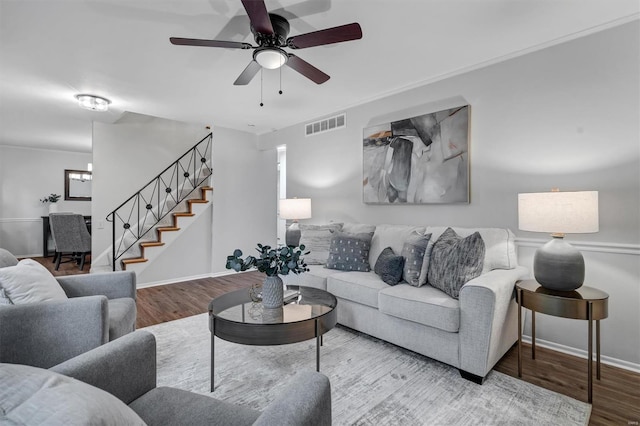 living room featuring stairs, ceiling fan, visible vents, and wood finished floors