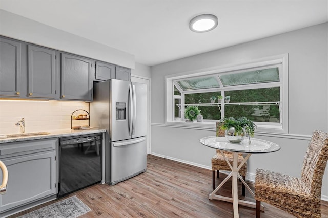 kitchen featuring stainless steel refrigerator with ice dispenser, dishwasher, a sink, gray cabinetry, and light wood-style floors