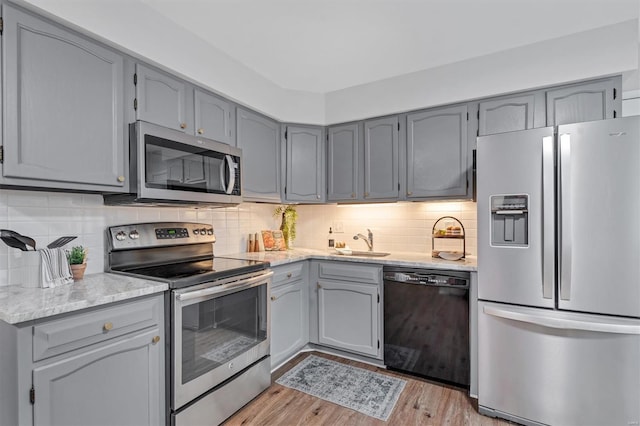 kitchen featuring gray cabinetry, appliances with stainless steel finishes, light wood finished floors, and a sink