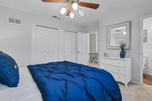 bedroom featuring two closets, light colored carpet, visible vents, and connected bathroom