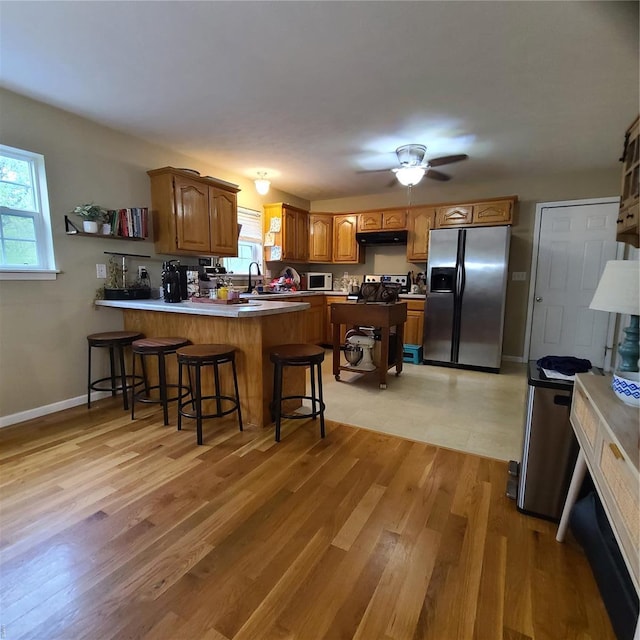 kitchen with a peninsula, under cabinet range hood, brown cabinets, a sink, and appliances with stainless steel finishes
