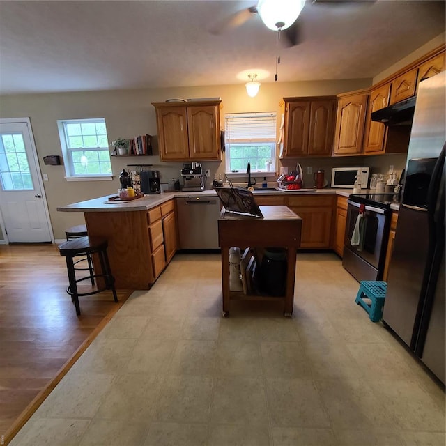 kitchen featuring a peninsula, under cabinet range hood, a healthy amount of sunlight, and stainless steel appliances