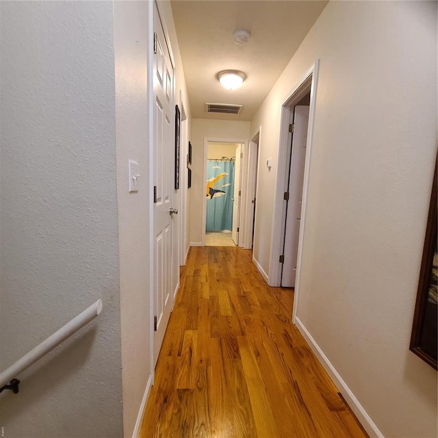 hallway featuring baseboards, visible vents, and wood finished floors