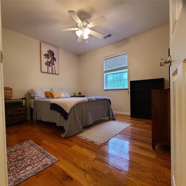 bedroom featuring baseboards, ceiling fan, wood finished floors, and visible vents