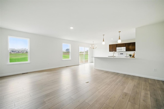 unfurnished living room with visible vents, light wood-type flooring, recessed lighting, a sink, and a notable chandelier