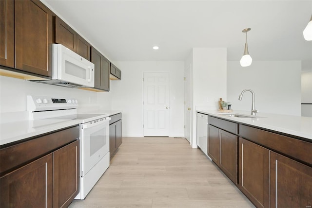 kitchen featuring pendant lighting, white appliances, light countertops, a sink, and light wood finished floors