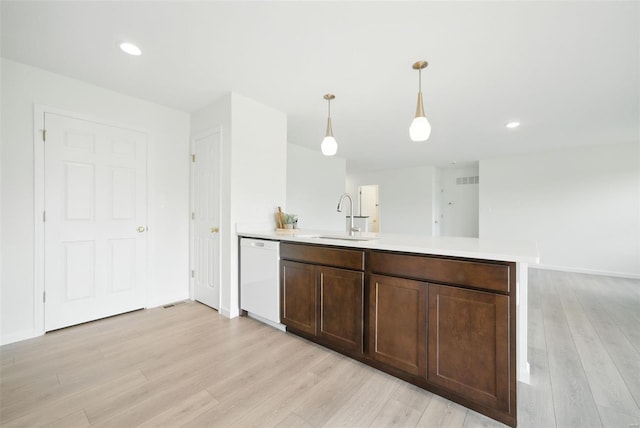 kitchen featuring a peninsula, white dishwasher, light countertops, a sink, and light wood-style flooring