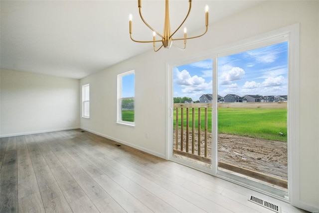 unfurnished dining area featuring baseboards, a notable chandelier, wood finished floors, and visible vents