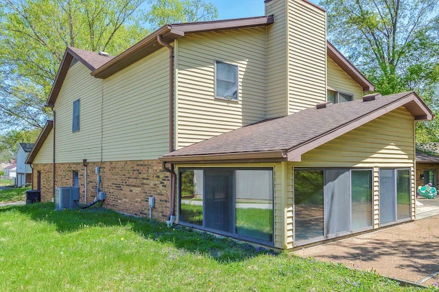 view of side of property with roof with shingles, brick siding, central AC unit, a chimney, and a yard