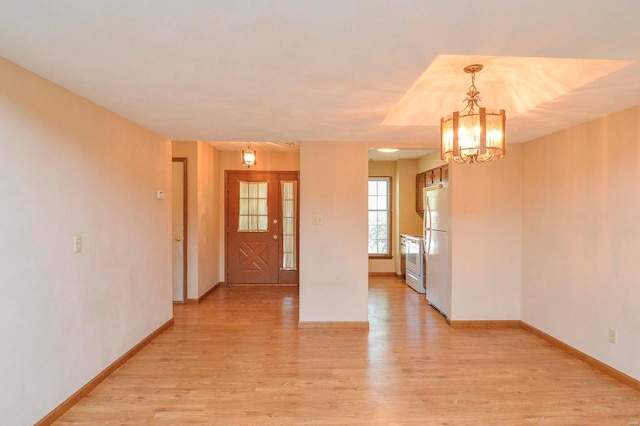 empty room featuring baseboards, light wood-type flooring, and a chandelier