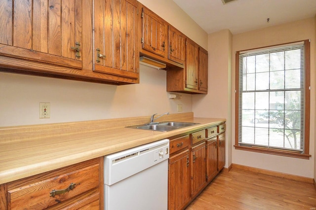 kitchen with brown cabinets, white dishwasher, a sink, light wood-style floors, and baseboards