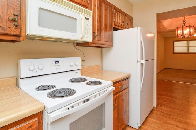 kitchen with brown cabinets, light countertops, a notable chandelier, white appliances, and light wood-style flooring