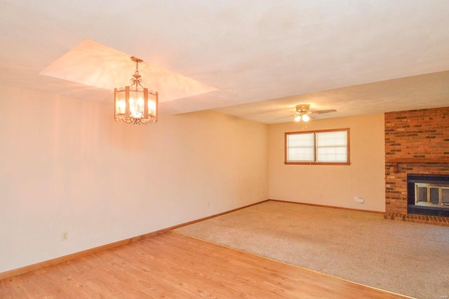 unfurnished living room with baseboards, ceiling fan with notable chandelier, and a brick fireplace