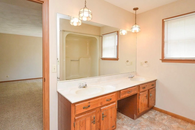 full bath featuring double vanity, baseboards, walk in shower, and a sink