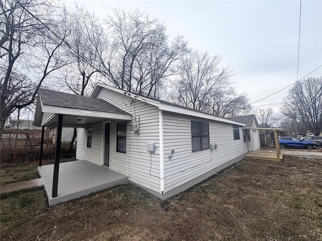 view of side of property with a patio area and roof with shingles
