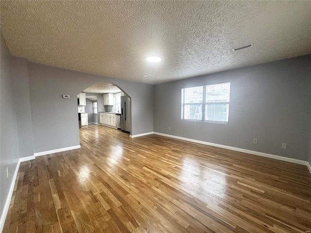 unfurnished living room featuring arched walkways, a textured ceiling, dark wood finished floors, baseboards, and visible vents