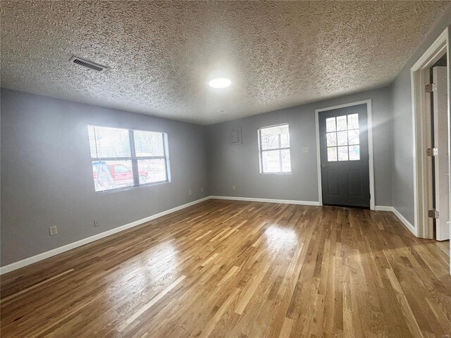 foyer entrance featuring visible vents, a textured ceiling, baseboards, and wood finished floors