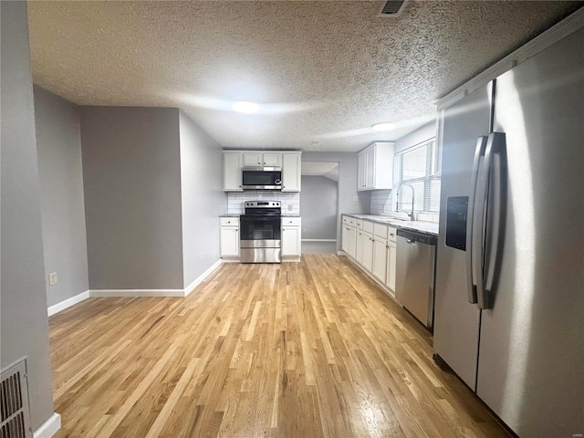 kitchen with white cabinetry, a sink, light wood-style flooring, backsplash, and stainless steel appliances