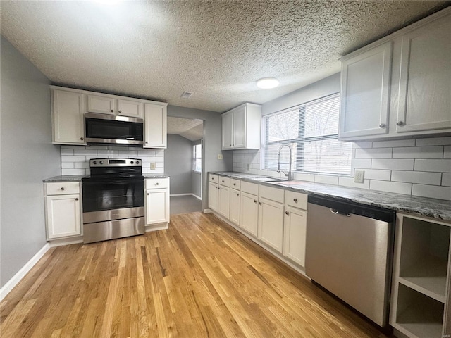 kitchen with decorative backsplash, a sink, baseboards, stainless steel appliances, and light wood-style flooring