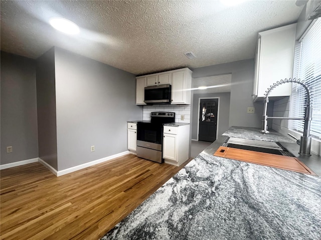 kitchen with visible vents, appliances with stainless steel finishes, wood finished floors, a sink, and white cabinetry