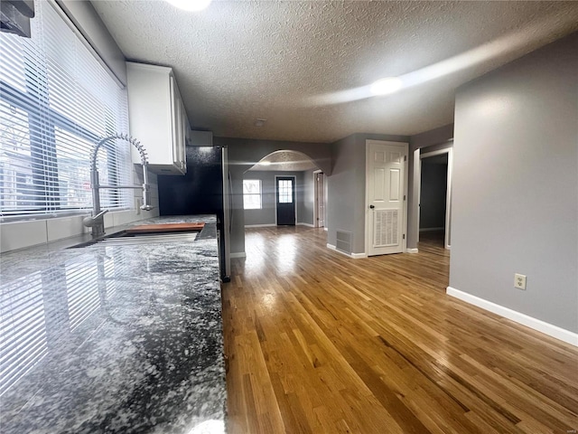 unfurnished living room with a sink, arched walkways, a textured ceiling, baseboards, and wood finished floors