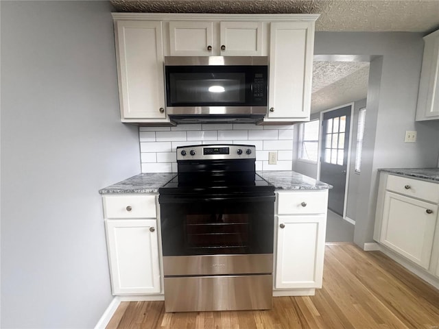 kitchen with baseboards, light wood-type flooring, a textured ceiling, tasteful backsplash, and appliances with stainless steel finishes