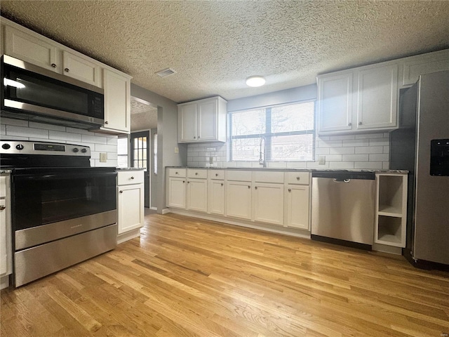 kitchen featuring white cabinets, appliances with stainless steel finishes, a sink, light wood-style flooring, and tasteful backsplash